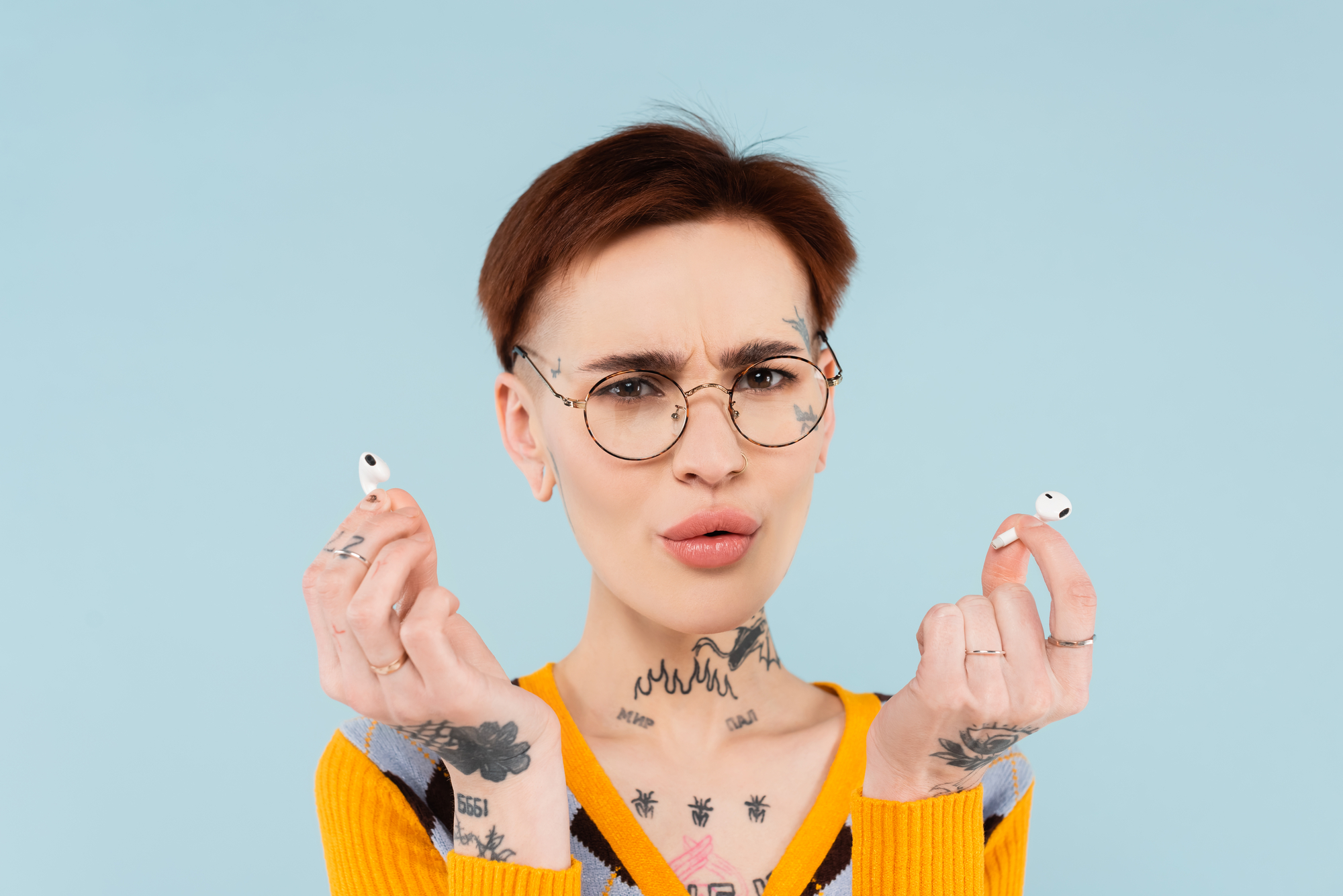 Surprised and tattooed woman in glasses holding wireless earphones
